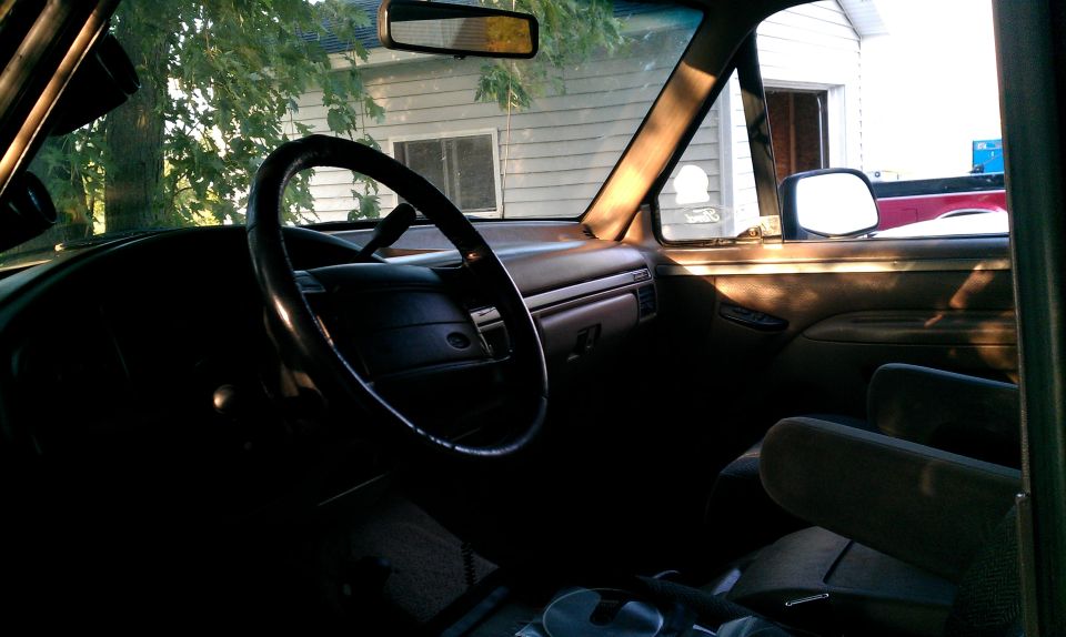 Vehicle interior with dashboard, steering wheel, and seats visible; sunlight streams through the windows