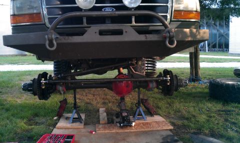 1995 Ford Bronco - The front axle and suspension of a 1995 Ford Bronco are visible, supported by jack stands and a floor jack.