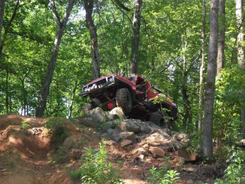 1987 Ford F-250 - This red truck navigates a rocky incline on a wooded trail, its off-road capabilities.