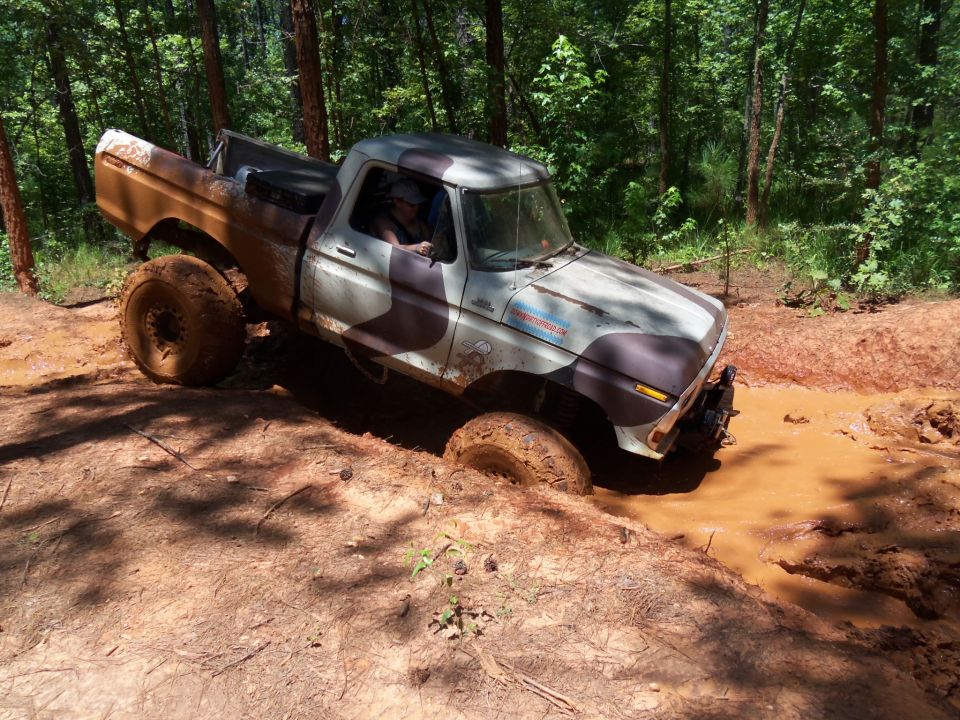 Mud-covered 1977 Ford F-150 stuck in a mud pit on a wooded trail