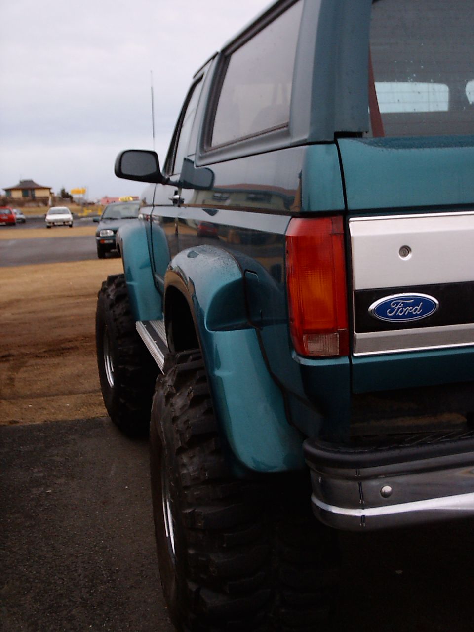 Rear corner of lifted teal Ford SUV on big mud tires with Ford tailgate badge