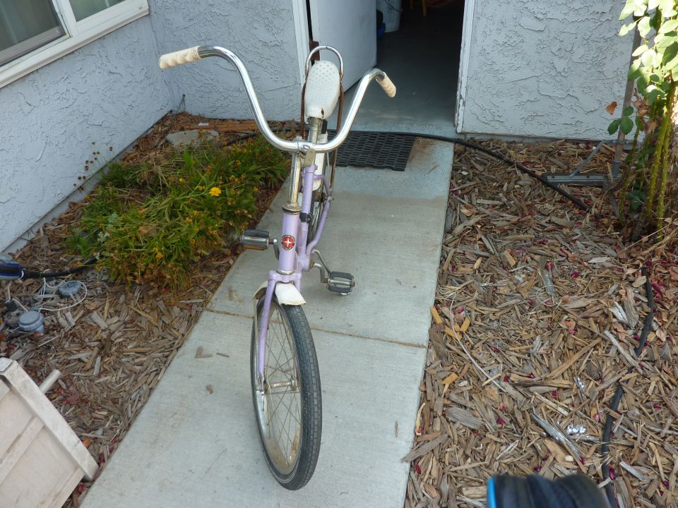 Purple bicycle with white grips and seat, parked on a sidewalk