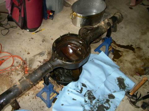 1995 Ford Bronco - A disassembled rear axle assembly rests on jack stands, surrounded by tools and spilled fluids on a concrete floor.