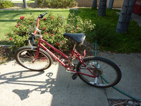 1900 Yugo GVX - A red bicycle is shown from the side, parked outdoors on a sunny day.