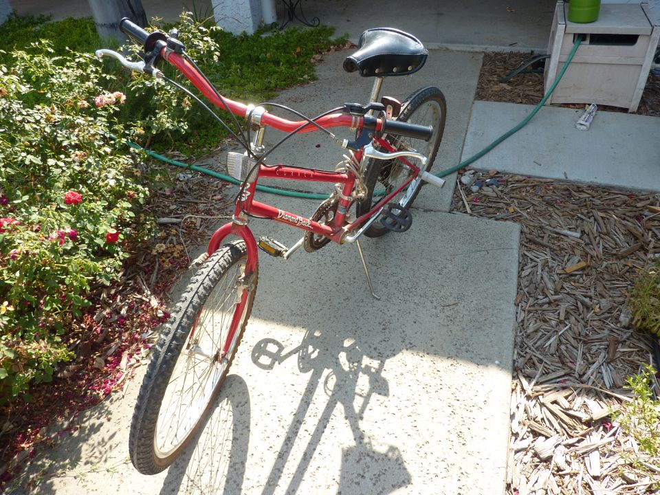 Red bicycle with black seat and handlebars, parked on a concrete path