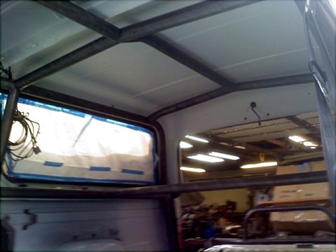1996 Ford Bronco - The interior of a vehicle shows a custom roll cage structure, with a taped-up window revealing an outdoor scene.