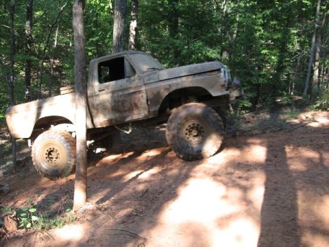 1979 Ford F-150 - A heavily muddied pickup truck navigates a steep, wooded trail.