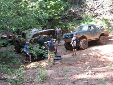 1979 Ford F-150 - Two off-road vehicles are stuck in a wooded area, with people working on one of them.