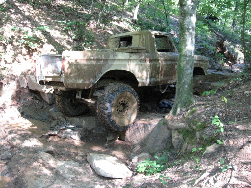 Mud-covered 1979 Ford F-150 navigating a rocky, muddy trail