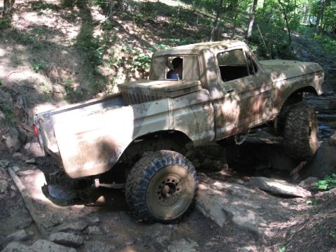 1979 Ford F-150 - This heavily soiled pickup truck is shown traversing a challenging, rocky terrain with a driver visible inside.