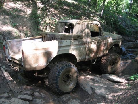 1979 Ford F-150 - A heavily modified 1973 Ford F-150 pickup truck is shown off-roading through a wooded, rocky area.