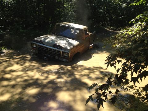 1979 Ford F-150 - Muddy 1979 Ford F-150 stuck deep in a water-filled trail, surrounded by trees.