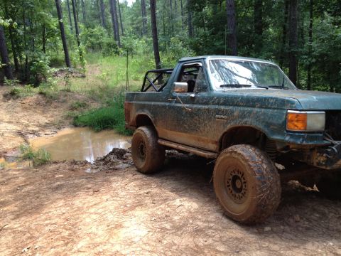 1979 Ford F-150 - This heavily modified off-road truck navigates a muddy trail through a wooded area.