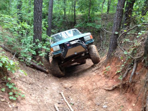 1979 Ford F-150 - Off-road vehicle with modified front end climbs a steep, muddy incline in a wooded area.