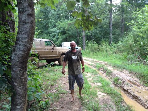 1979 Ford F-150 - A man walks down a muddy trail past a tan Ford Bronco and another vehicle in a wooded area.