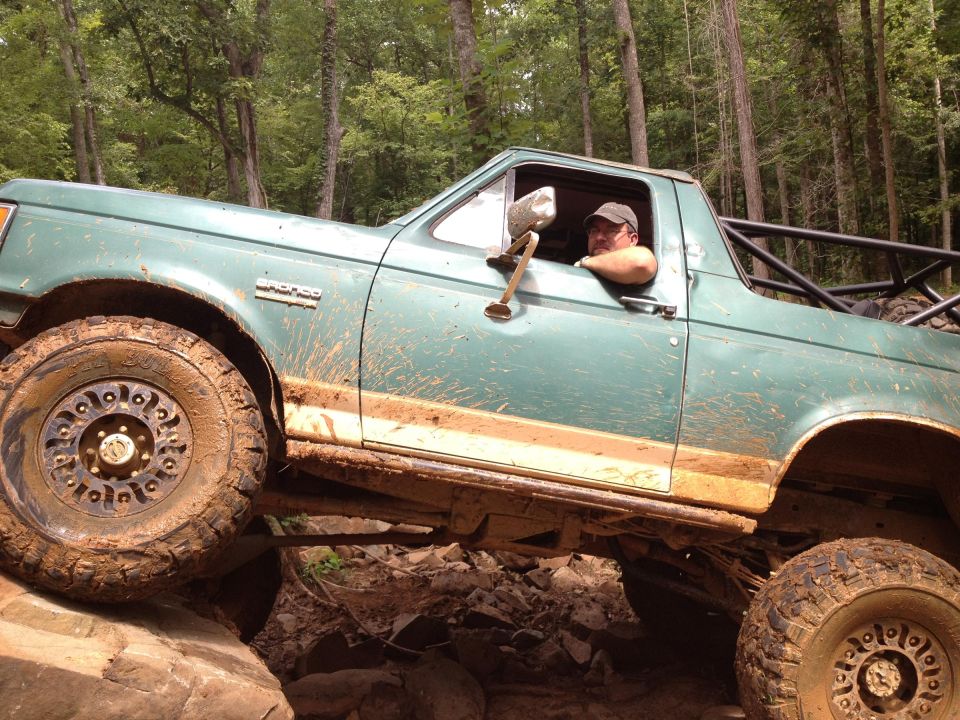 Green Ford Bronco with roll cage off-roading over rocks, driver visible