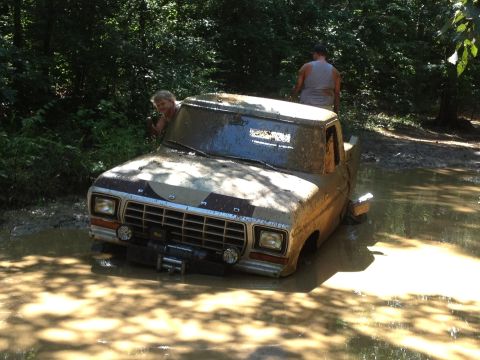 1979 Ford F-150 - A muddy 1979 Ford F-150 is stuck in water, with two people visible around the vehicle.