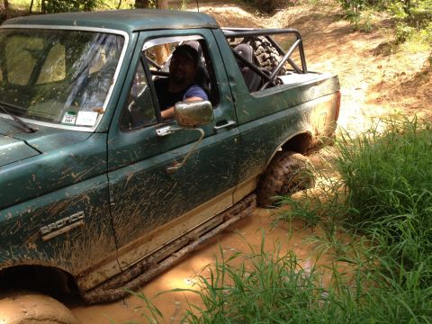 1979 Ford F-150 - A green Bronco is stuck in a muddy trail with grass on the side. The driver is visible behind the wheel.