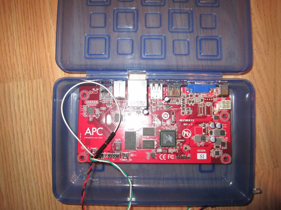 Red circuit board with 'APC' logo and various ports, inside a blue plastic case