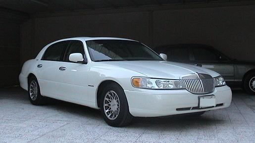 White Lincoln Town Car sedan parked in a carport, vertical chrome grille and lace-spoke wheels