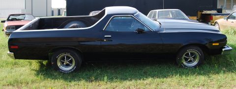 1975 Ford Ranchero - A black 1975 Ford Ranchero is parked on a grassy area with other vehicles in the background.