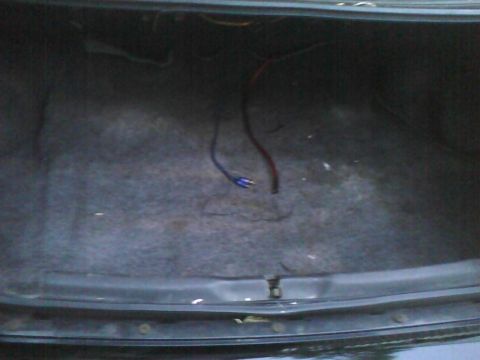 2003 Ford Crown Victoria - The interior of a car's trunk shows a worn carpet and some loose electrical wires.