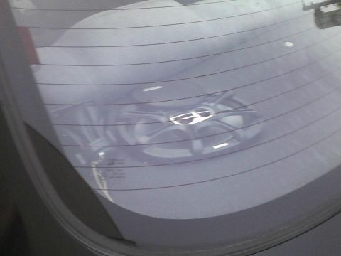 2003 Ford Crown Victoria - A car wheel with a silver emblem is visible through the rear window of a vehicle.