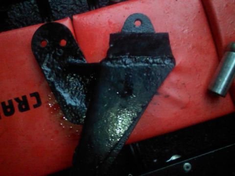 1993 Ford F-150 - A close-up view of a welded metal bracket, likely a vehicle part, resting on a red surface with visible text.