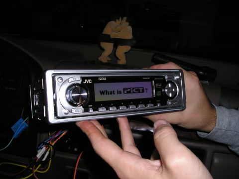 1996 Ford Bronco - Hands installing a JVC CD/MP3 player into a car dashboard, with a sumo wrestler figurine on top.