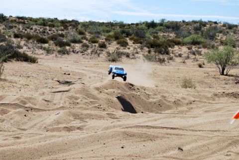 1986 Ford Bronco - Remote control truck airborne over a sandy terrain, with a desert landscape in the background.
