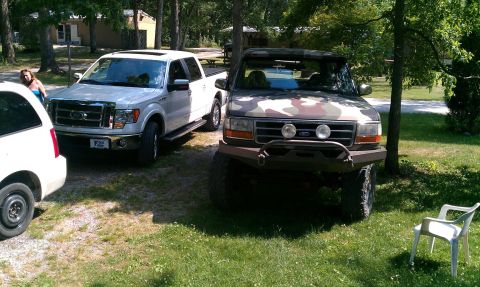 1995 Ford Bronco - A camouflaged Ford Bronco is parked next to a white pickup truck in a grassy area.