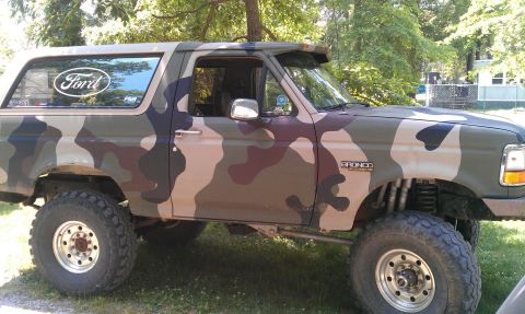 1995 Ford Bronco - Camouflaged 1995 Ford Bronco with lifted suspension and off-road tires parked outdoors.