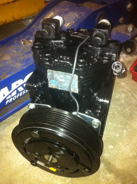 1989 Ford Bronco - A black AC compressor with a pulley is shown, resting on a blue car jack.