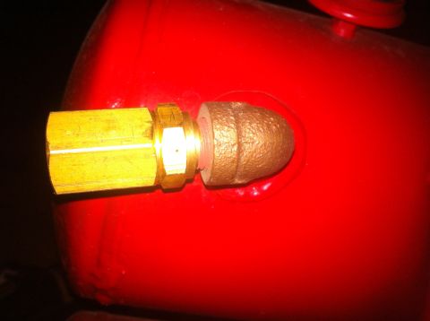 1989 Ford Bronco - Close-up of a brass fitting attached to a red tank, with a bronze cap on the end.