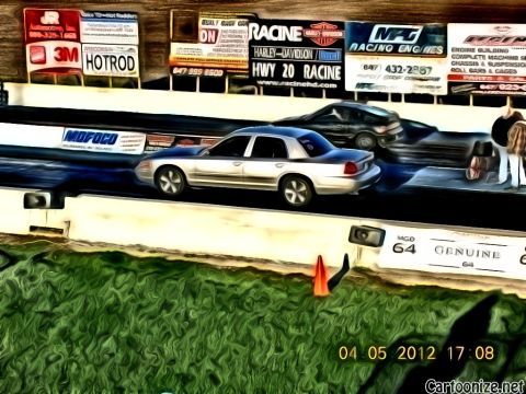2003 Ford Crown Victoria - A silver sedan, likely a 2003 Ford Crown Victoria, races down the drag strip with another vehicle visible.