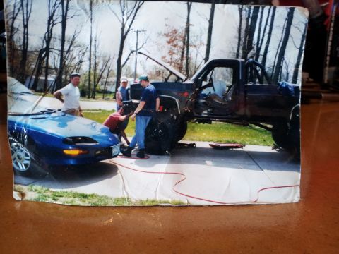 1978 Chevrolet C/K Pickup - Two vehicles are present, a blue Camaro and a lifted pickup truck, with several people gathered around the truck.