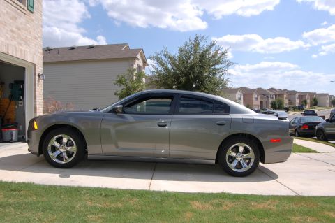 2012 Dodge Charger - Side view of a gray sedan parked on a concrete driveway under a cloudy sky.