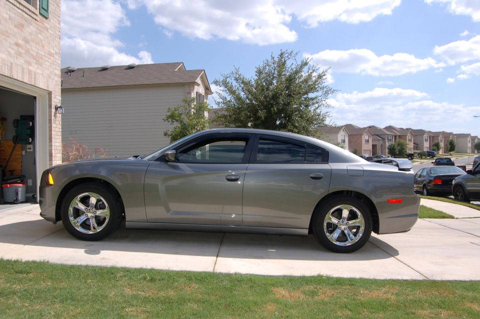 Gray sedan parked in a driveway next to a garage. Houses and trees in background
