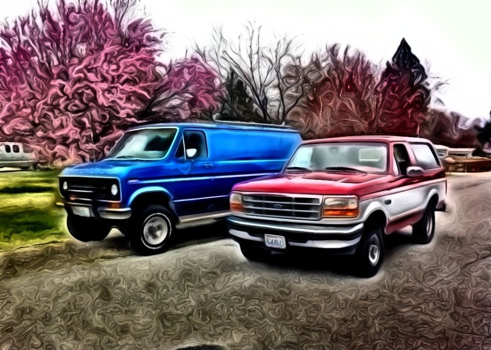 Red and white Ford Bronco 3/4 front view next to blue van