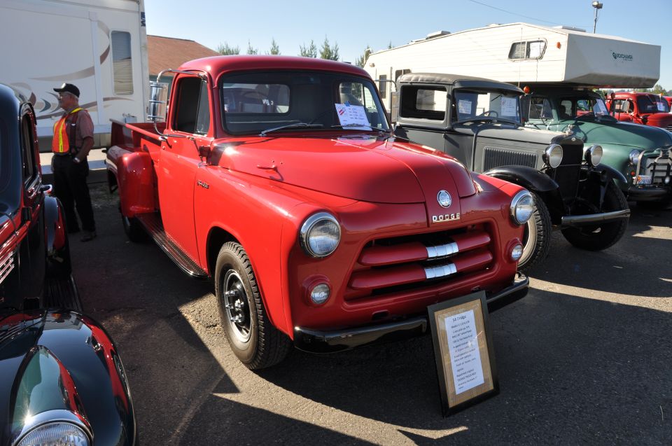 Red Dodge pickup truck parked next to other vintage vehicles. A sign is in front of the truck