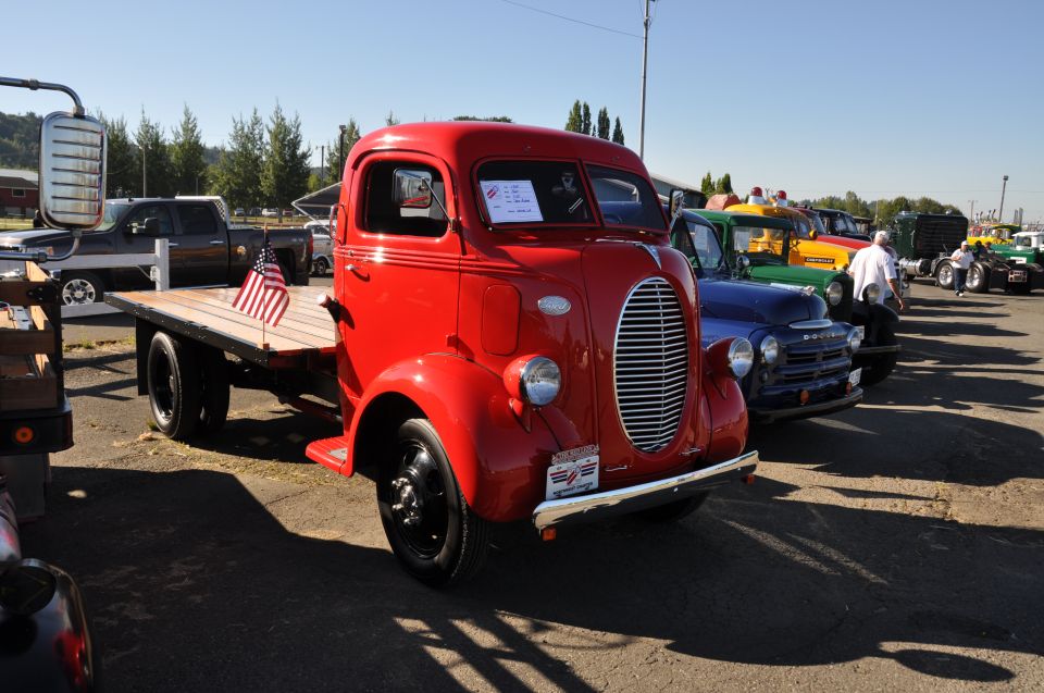Red flatbed truck with an American flag on the bed, parked in a line with other trucks