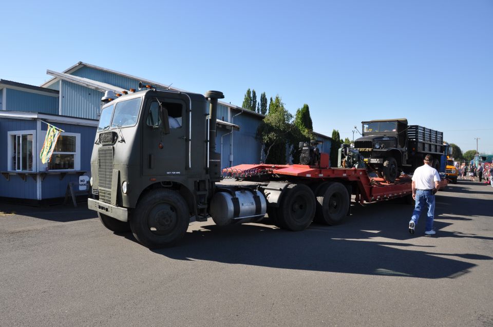 Army green semi-truck towing a military truck on a red flatbed trailer