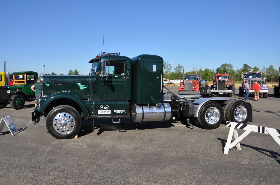 Dark green semi-truck parked next to other trucks. Text on the truck reads 'The Green Machine'