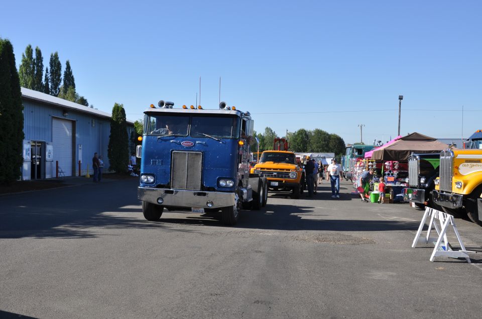 Blue Peterbilt truck parked outside a building, with other trucks and people in the background