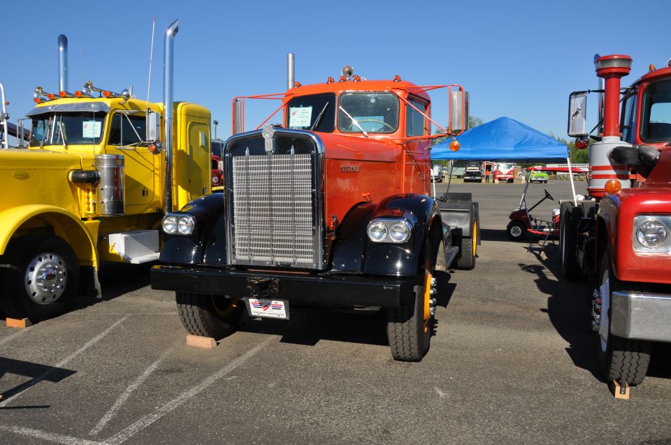 Orange and black 1959 Kenworth W900A truck parked between other trucks