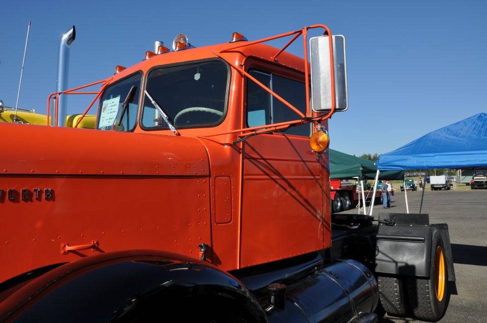 Close-up of an orange semi-truck cab. Text on the door reads 'KENWORTH'