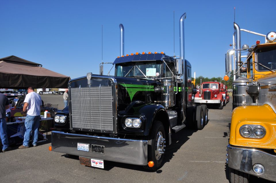 Black semi-truck with green stripes and chrome grille, parked next to other trucks