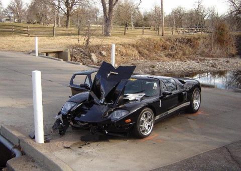 2007 Ford Mustang - A black Ford GT sustained front-end damage and has its hood open, resting on a concrete surface next to a small stream.