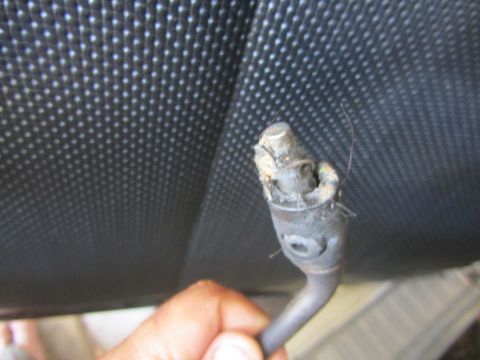 1964 Ford Ranchero - A hand holds a broken shifter cable, showing damage to the end, against a textured black background.