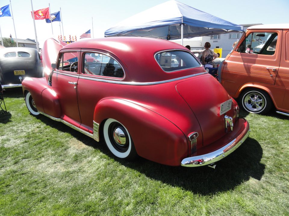 Red sedan with hood up parked next to an orange van. Flags are flying in the background